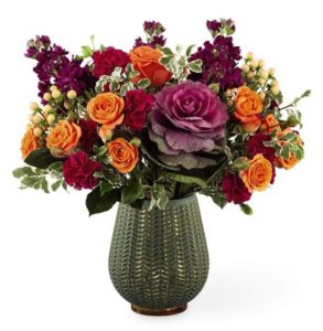 red and orange roses with green and purple accents in vase