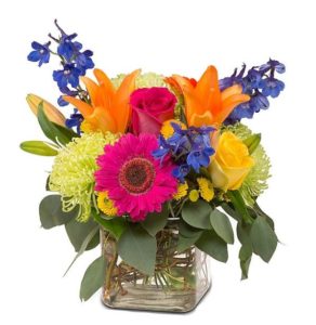 Roses, lilies, delphimium, mums and more arranged together to create this beautiful and colorful bouquet presented in a glass cube vase.