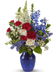 Beautiful red, white and blue blossoms which include roses, carnations, snapdragons and more arrive in a lovely cobalt blue vase.